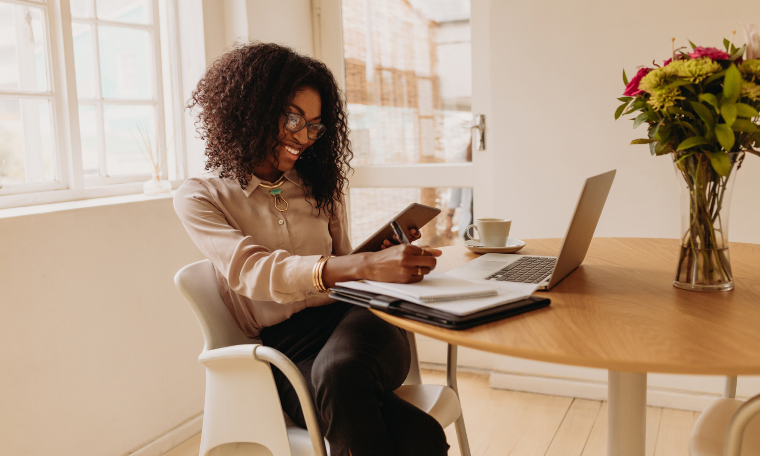 Photo of a woman working from home with laptop, notepad and pen and mobile phone.