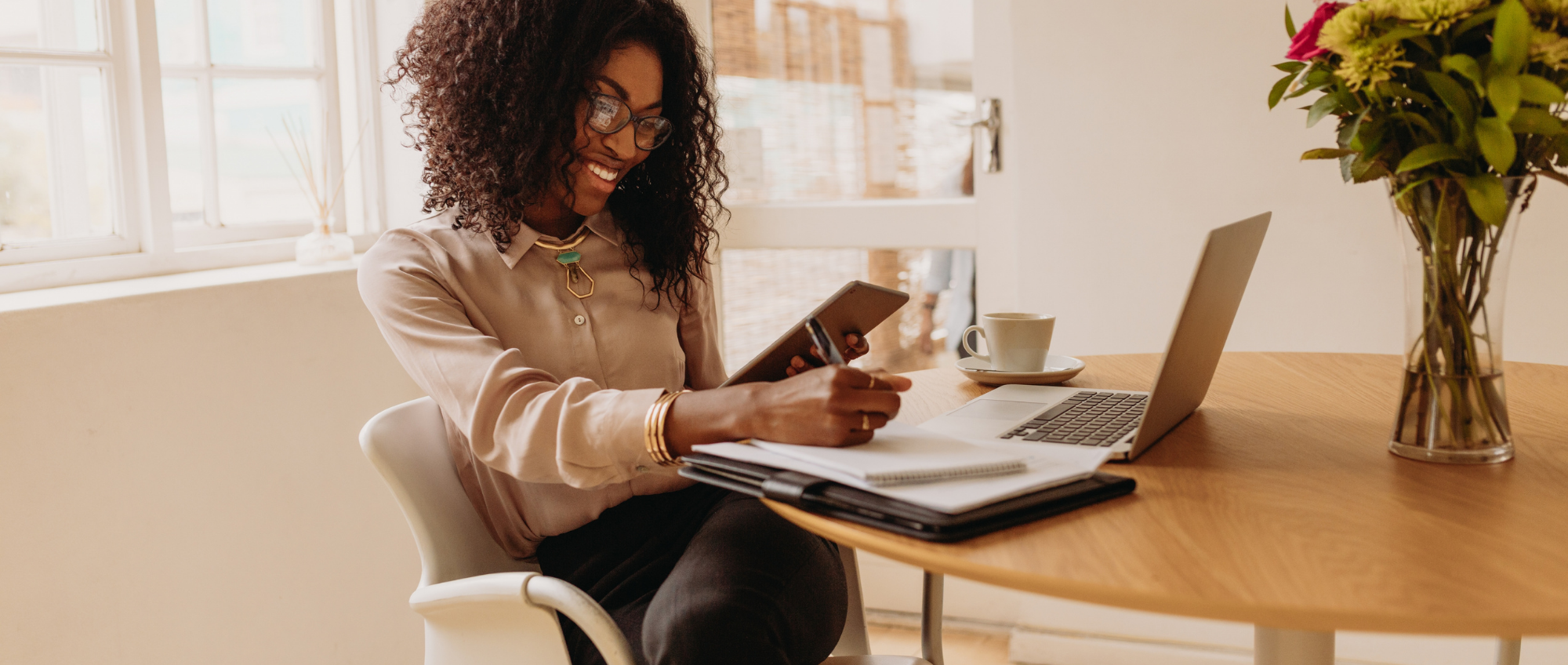 Photo of a woman working from home with laptop, notepad and pen and mobile phone.
