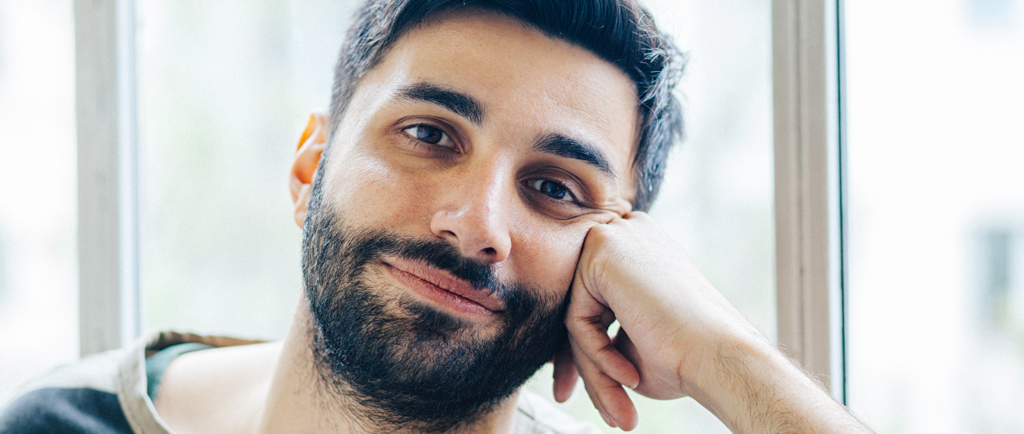 Photo of a man looking down the camera, leaning his face on his cheek.