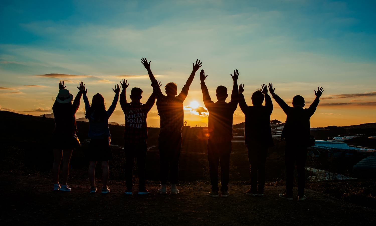 photo of people with their hands in the air in front of a sunset