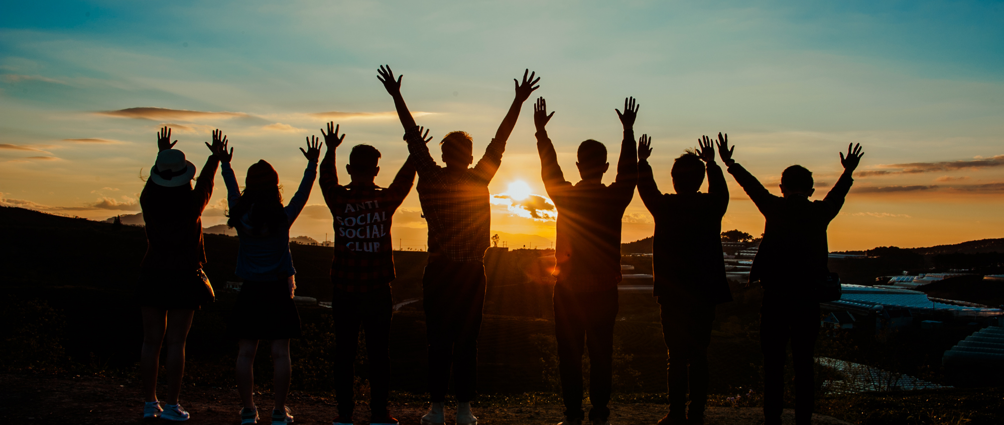 photo of people with their hands in the air in front of a sunset