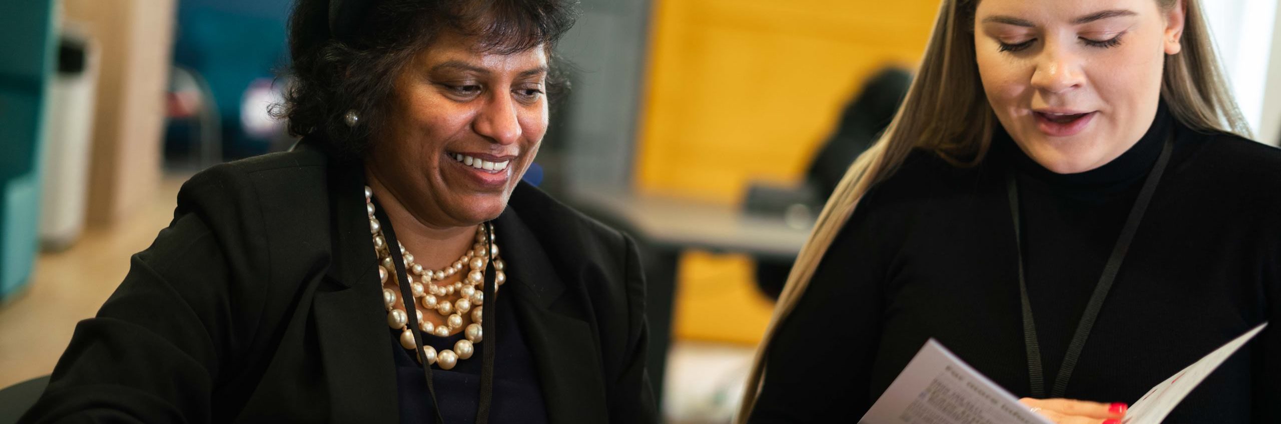 Two women sat at a desk looking at a brochure