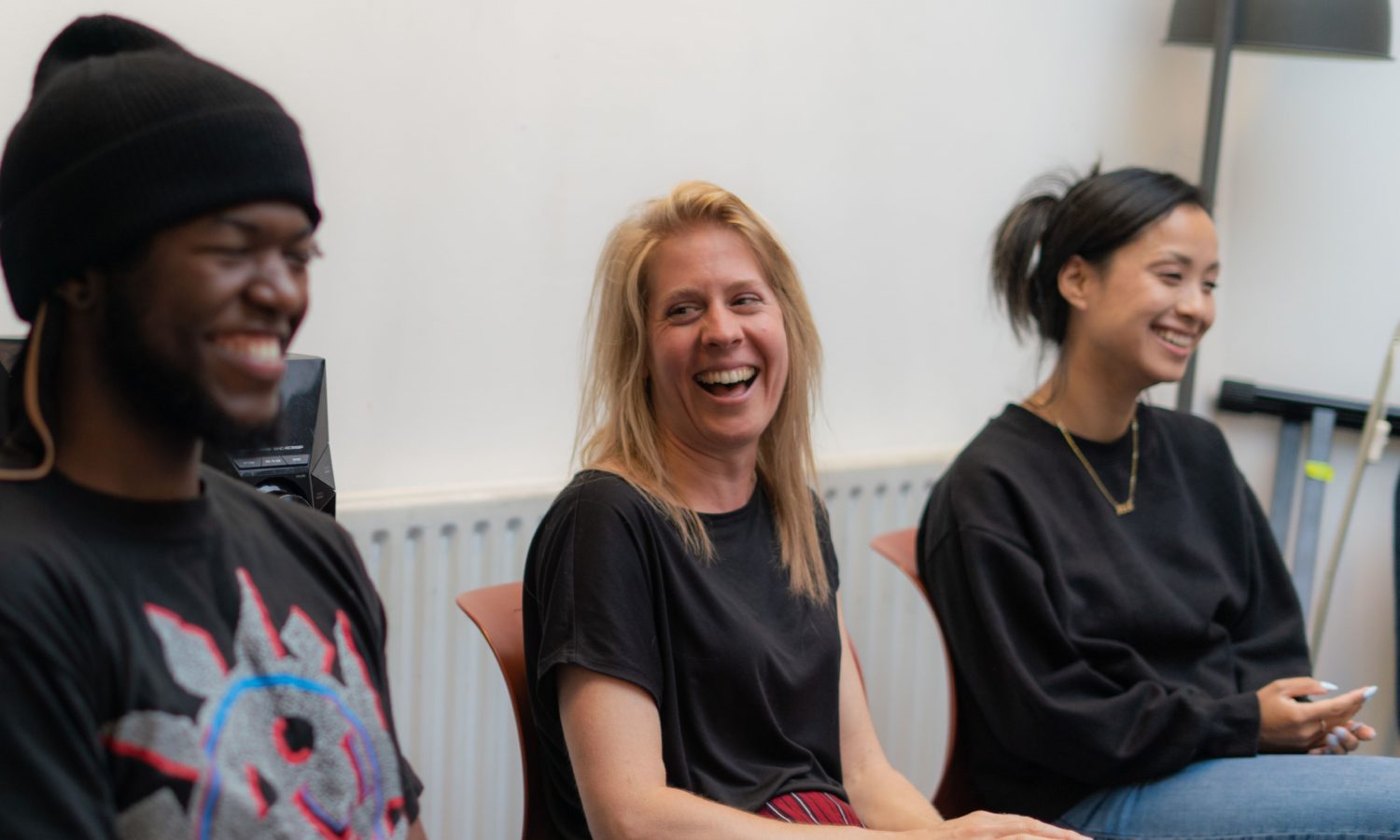 Three people of varying ages sat down. They are smiling and laughing happily. They are in an informal setting.