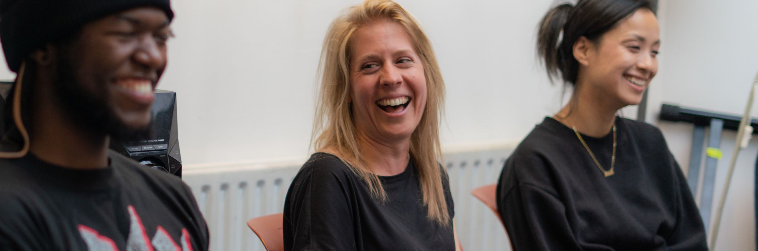 Three people of varying ages sat down. They are smiling and laughing happily. They are in an informal setting.