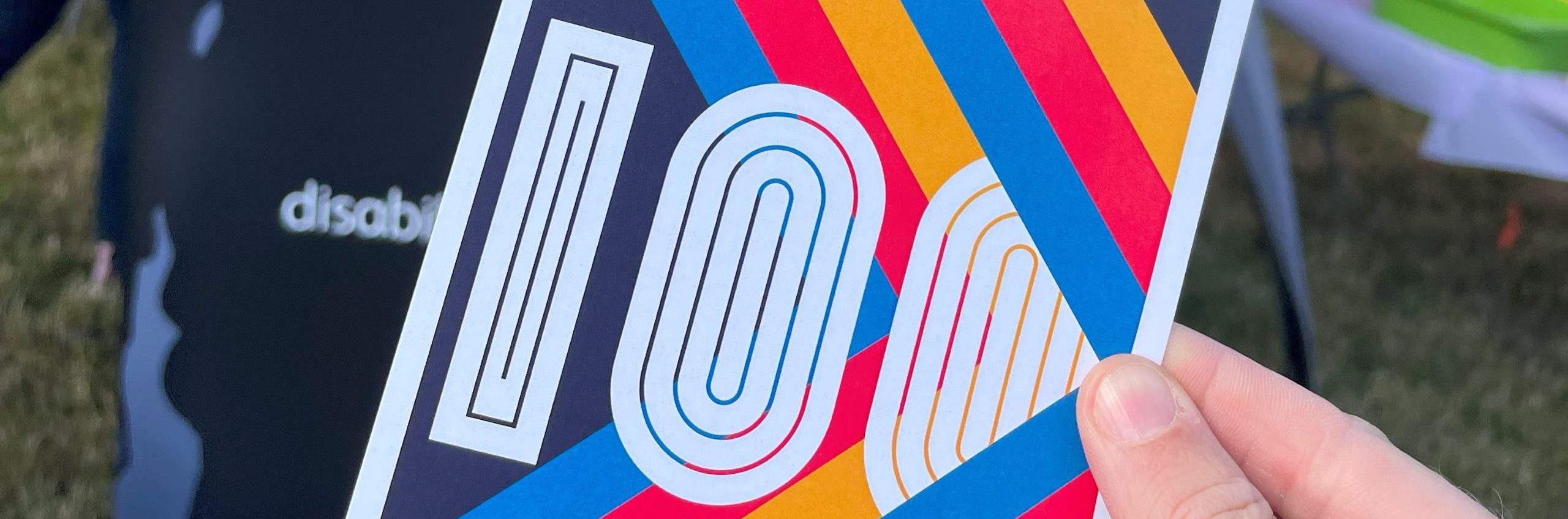a retro, 70s inspired DP100 postcard with coloured stripes and 100 across the middle.