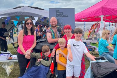 A family stand in front of the DP100 banner at the Shaw Trust stand.