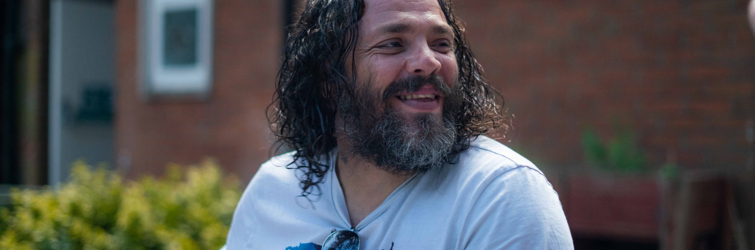 Close up photo of man with curly hair, sat outside smiling.