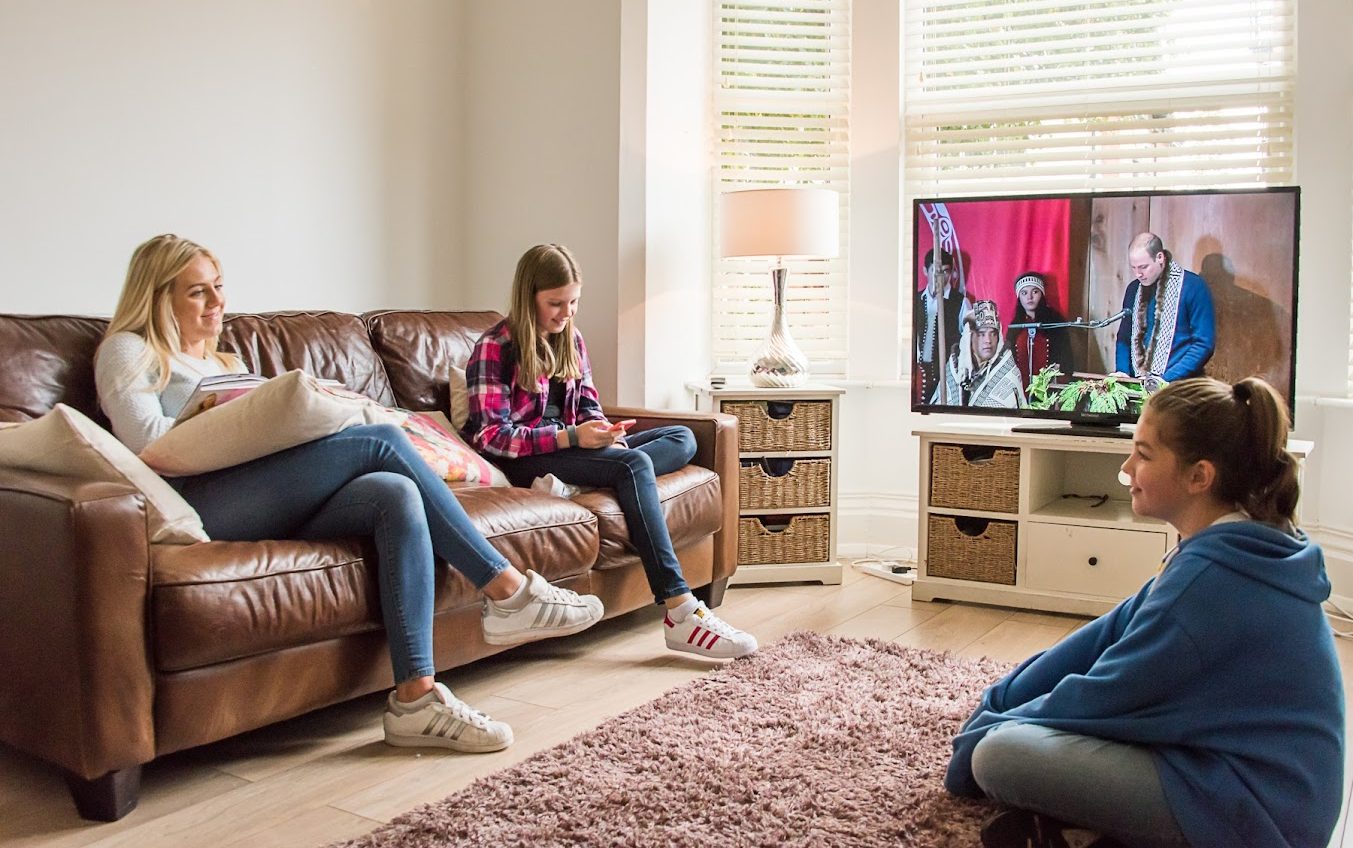 Three people sat in a cosy living room watching TV